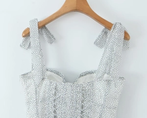 Detail of white polka dot dress featuring adjustable bow tie straps and drawstring bust