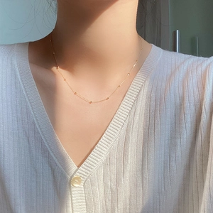 Gros plan d'un collier ras du cou en perles dorées minimaliste porté par un mannequin