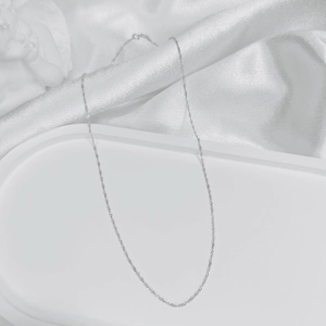 Elegant close-up of a minimalist silver O-chain necklace on a white silk background