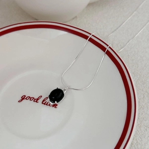 Macro detail of black onyx oval pendant with silver snake chain on white ceramic plate