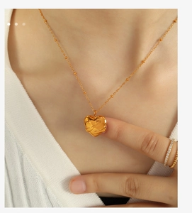 Detailed view of a gold 18K plated heart pendant necklace and matching rings on a model