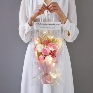 Detail of carnation bouquet in transparent gift bag with warm LED fairy lights