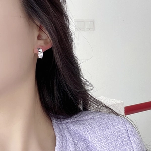 Close-up of geometric faceted silver earrings on ear showing delicate texture