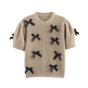 Gros plan sur la texture en maille et les nœuds en satin noir du pull-over de couleur beige