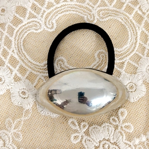 Detail of minimalist hair tie with silver oval metal bead on white lace fabric