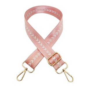 Close-up of pink nylon bag strap with arrow pattern and gold adjustable buckle clips
