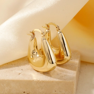 Polished gold U-shaped drop earrings displayed on stone base with satin background