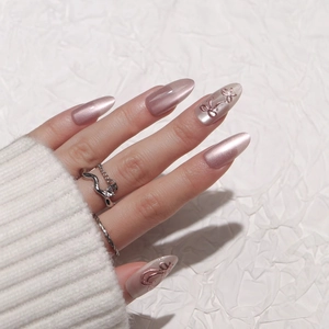 Pink cat eye press-on nails with 3D metallic bow charms on long almond shaped tips