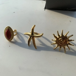 Close-up of three gold-plated rings featuring red agate, starfish, and sun motifs