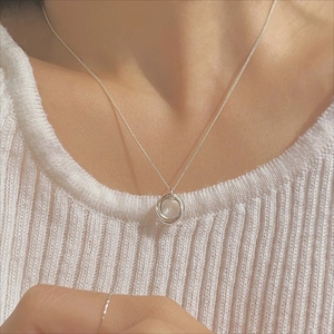 Detail of interlocking triple circle silver necklace worn over a white knit sweater