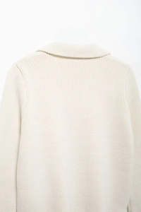 Gros plan du dos d'un cardigan crème montrant la maille côtelée et le détail du col à revers