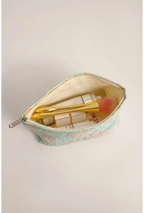 Dettaglio di un beauty case jacquard a fiori con pennelli e prodotti di bellezza