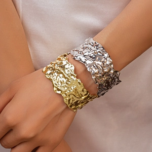 Detail of wide metal cuff bracelets in gold and silver with molten lava texture finish