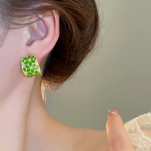Close-up of green and gold C-shaped floral earrings featuring a textured enamel honeycomb pattern