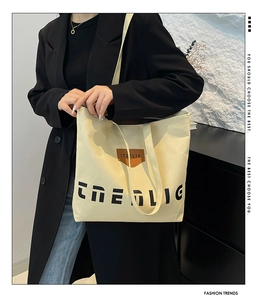Detail of off-white canvas tote bag with black lettering and leather logo patch