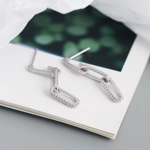 Macro detail of silver geometric chain earrings with zircon inlay on a white book
