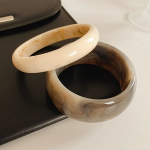 Close-up of resin bangles in cream and marble brown textures on black leather