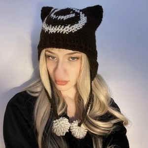 Detail of hand-knit cat ear beanie with white spiral patterns and plush pom-pom ties