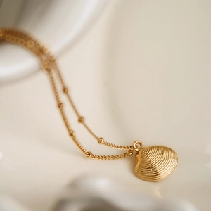Macro shot of gold shell pendant with radiating texture and beaded satellite chain