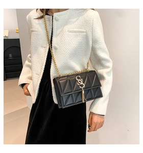 Close-up of quilted black PU leather bag with gold S-logo and fringe on white jacket