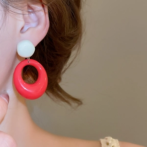 Gros plan d'un modèle portant des boucles d'oreilles ovales en résine rouge et blanche