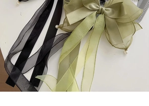 Detail of satin bow hair clip with organza layers, flowing tassels and pearl beads