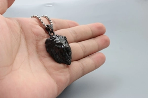 Close-up of a hand holding a black lion head pendant with a silver metal necklace chain