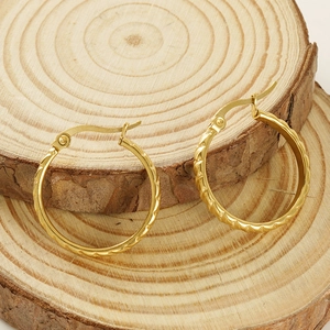 Detailed view of gold hoop earrings with diamond textured patterns on wooden slice