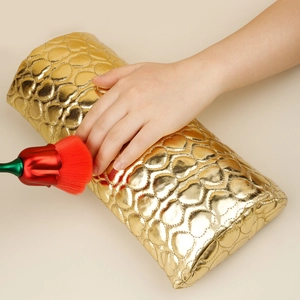 Close-up of golden PU leather manicure hand rest with heart-shaped quilting and brush