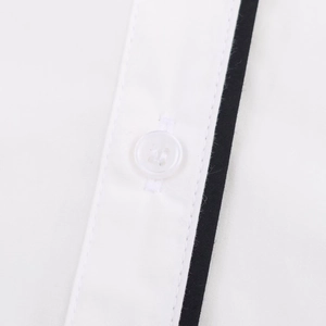 Detailed close-up of white poplin shirt with black contrast trim and four-hole button