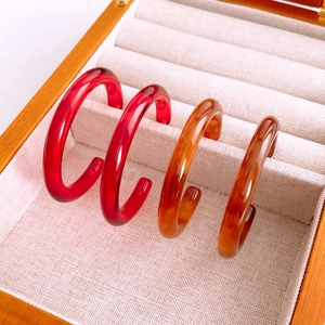 Close-up of red and amber resin C-shape earrings displayed in a velvet jewelry box