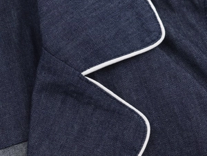 Macro detail of navy blue denim jacket with contrast white piping on lapel and seams