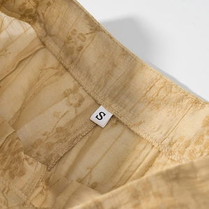 Detailed macro view of light gold jacquard fabric texture and size S tag on waistband