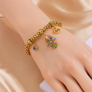 Gold beaded Hamsa and Evil Eye charm bracelet with colorful enamel details on silk background