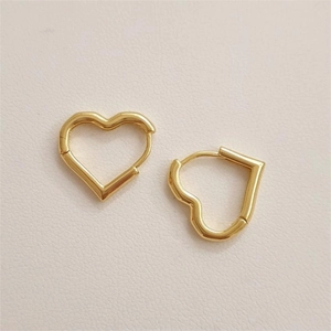 Polished gold heart-shaped huggie hoop earrings on a textured cream leather background