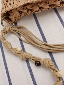 Handwoven straw beach bag with wooden beads and bronze rings on striped fabric background