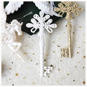 Close-up of resin Pegasus and golden key Christmas ornaments on white plush background