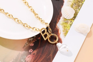 Close-up of gold chunky chain necklace with B letter pendant and baroque pearl detail