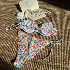 Detaillierte Flachbildaufnahme des Floral-Bikinis mit Bügel-Top und Bindehose auf Strohmatte