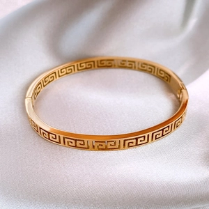 Vintage golden titanium steel bangle with classic Greek meander pattern on white silk