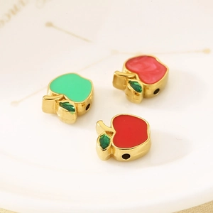 Macro detail of red and green enamel apple charms with gold edges for jewelry making