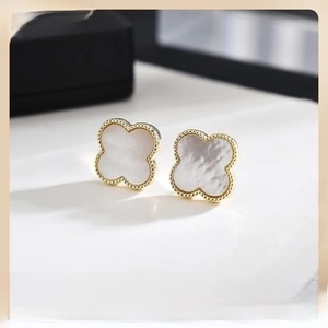 Macro shot of gold-plated clover earrings with white inlay and detailed bead edge