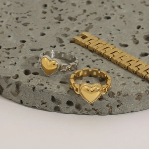 Detail of heart charm chain rings in gold and silver finish on natural stone background