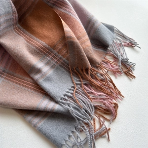 Detailed close-up of gray pink and caramel plaid scarf texture with fringed edges