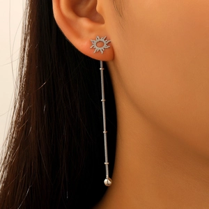 Detail of silver sun-shaped stud earring with long metal tassel on a female model