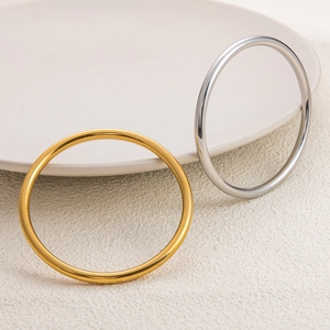 Polished minimalist 18K gold and silver stainless steel bangles on ceramic tray