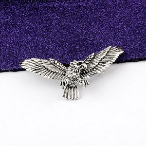 Detail of antique silver eagle brooch with textured feathers and green gemstone eye