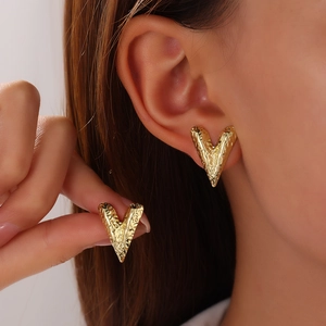 Macro view of gold-plated heart stud earrings with unique hammered texture on ears