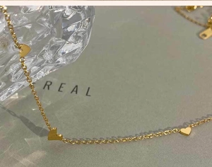 Primer plano del collar dorado con colgantes de corazón sobre cristal y luz suave