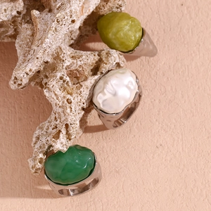 Detail of three chunky silver rings with irregular green and white acrylic stones on coral